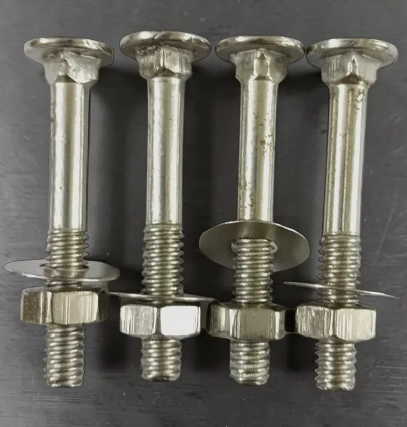 Four silver carriage bolts with washers and hex nuts standing upright